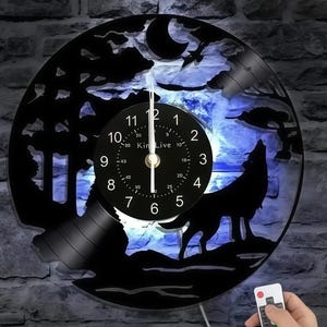 May include: Black vinyl record clock with a wolf howling at the moon design. The clock face is black with white numbers and hands. The clock is illuminated with blue light and includes a remote control.