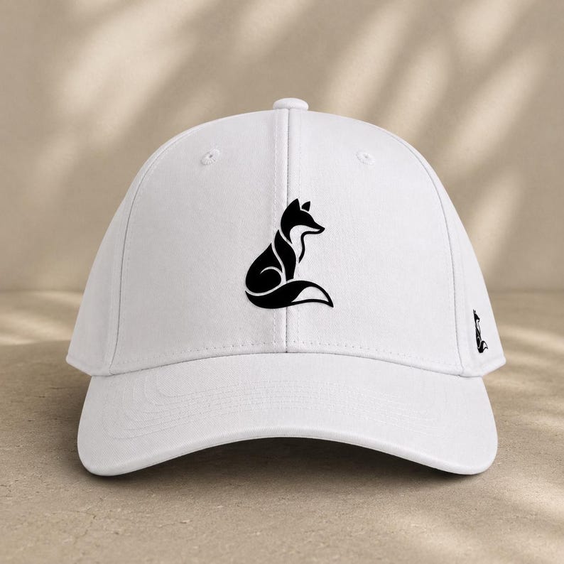 Pode incluir: Bon&eacute; de beisebol branco com uma silhueta de raposa preta na frente e um log&oacute;tipo de raposa menor na lateral. O bon&eacute; tem uma aba curva e uma al&ccedil;a ajust&aacute;vel. Um acess&oacute;rio elegante para atividades ao ar livre.
