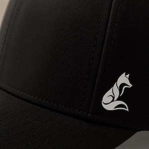 Pode incluir: Bon&eacute; de beisebol preto com um logotipo de raposa branco na lateral. O bon&eacute; &eacute; feito de um tecido dur&aacute;vel e apresenta uma aba curva. O logotipo da raposa &eacute; um design estilizado.