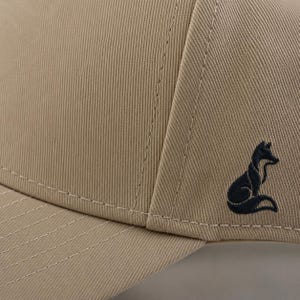 Pode incluir: Bon&eacute; de beisebol bege com um log&oacute;tipo de raposa bordado a preto na lateral. O bon&eacute; tem uma coroa estruturada, uma aba curva e costuras vis&iacute;veis. O tecido tem uma textura canelada.