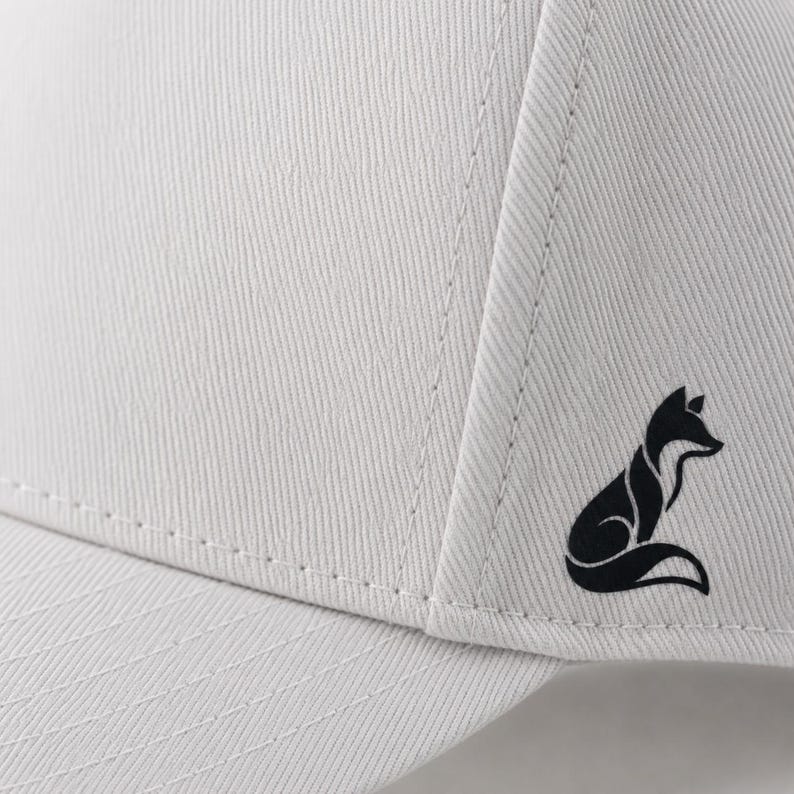 Pode incluir: Bon&eacute; de beisebol cinza claro com um logotipo de raposa preta na lateral. O bon&eacute; tem um design estruturado com costuras vis&iacute;veis e uma viseira curva. O logotipo da raposa &eacute; uma silhueta estilizada.