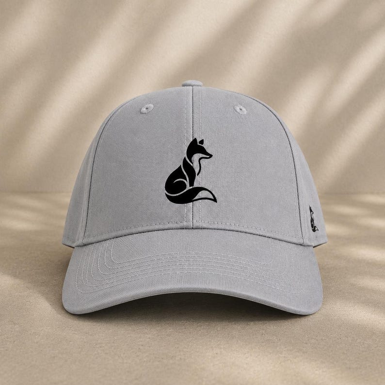 Pode incluir: Bon&eacute; de beisebol cinza claro com uma silhueta de raposa preta na frente. O bon&eacute; tem uma aba curva e um pequeno logotipo de raposa na lateral. O chap&eacute;u &eacute; feito de um tecido macio e texturizado.