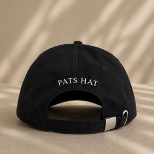 Pode incluir: Bon&eacute; de beisebol preto com o texto "PATS HAT" em branco. O bon&eacute; tem uma aba curva, um fecho de metal e uma al&ccedil;a de tecido para ajuste. O chap&eacute;u &eacute; feito de um material dur&aacute;vel.