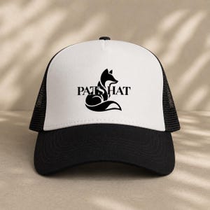 Op de afbeelding: Zwarte en witte truckerpet met de tekst "PATS HAT" en een zwart vossilhouet. De pet heeft een wit voorpaneel, een zwarte klep en een zwarte mesh achterkant.