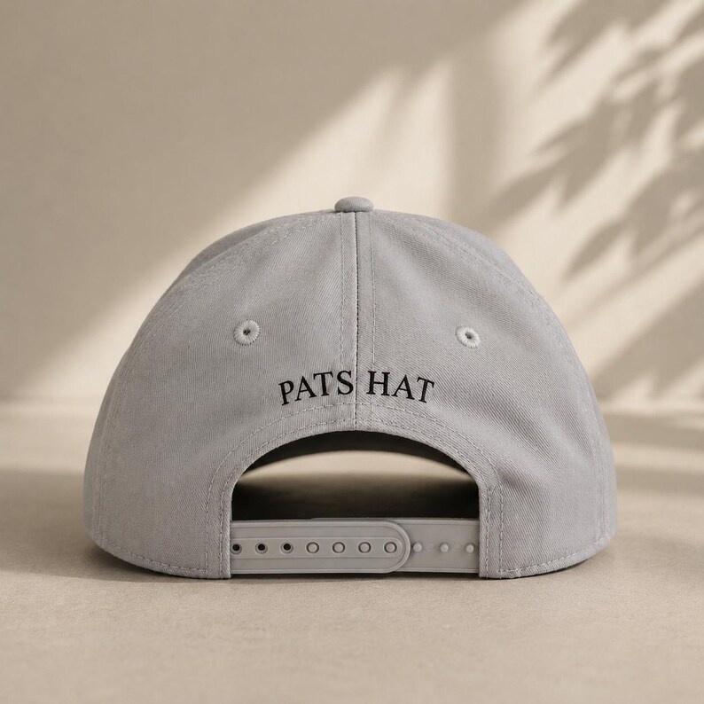 Pode incluir: Bon&eacute; de beisebol cinza claro com o texto "PATS HAT" em preto. O bon&eacute; tem uma aba curva e uma al&ccedil;a ajust&aacute;vel na parte de tr&aacute;s. Feito de um material macio e dur&aacute;vel.