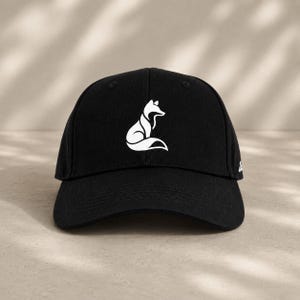 Pode incluir: Bon&eacute; de beisebol preto com um desenho de raposa branca. O bon&eacute; tem uma viseira curva e um design estruturado. O desenho da raposa &eacute; estilizado e minimalista.