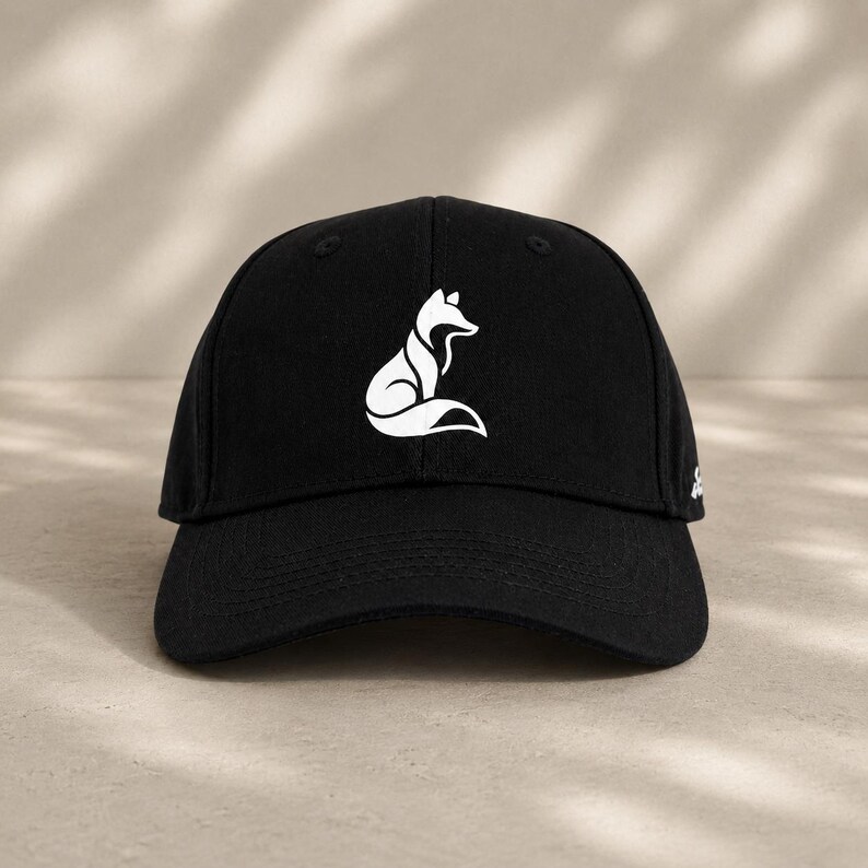 Pode incluir: Bon&eacute; de beisebol preto com um desenho de raposa branca. O bon&eacute; tem uma viseira curva e um design estruturado. O desenho da raposa &eacute; estilizado e minimalista.