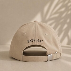 Pode incluir: Bon&eacute; de beisebol bege com o texto "PATS HAT" em preto. O bon&eacute; tem uma aba curva, um fecho de metal e um pequeno bot&atilde;o na parte superior. Feito de um material macio e dur&aacute;vel.
