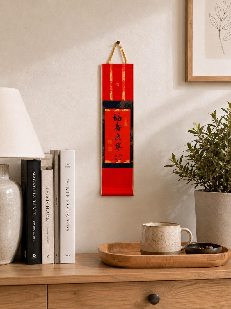 Mini red Chinese calligraphy wall scroll displayed in a cozy home setting with books, lamp, plant, and wooden shelf decor