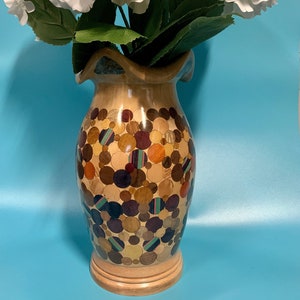 Puede incluir: Un jarr&oacute;n de madera con un dise&ntilde;o &uacute;nico que presenta un mosaico de c&iacute;rculos coloridos. El jarr&oacute;n est&aacute; lleno de flores de hortensia blancas.