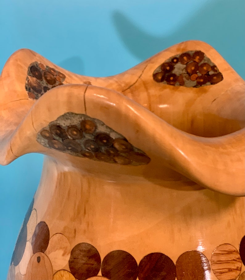 Puede incluir: Un jarr&oacute;n de madera con un dise&ntilde;o &uacute;nico y ondulado. El jarr&oacute;n est&aacute; hecho de madera clara con detalles marrones oscuros y un patr&oacute;n circular alrededor de la base.