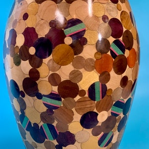 Puede incluir: Un jarr&oacute;n de madera con un dise&ntilde;o &uacute;nico. El jarr&oacute;n est&aacute; hecho de diferentes tipos de madera, cada uno con un color y una veta diferentes. La madera est&aacute; dispuesta en un patr&oacute;n circular, creando un dise&ntilde;o visualmente atractivo. El jarr&oacute;n es una pieza de arte hermosa y &uacute;nica.