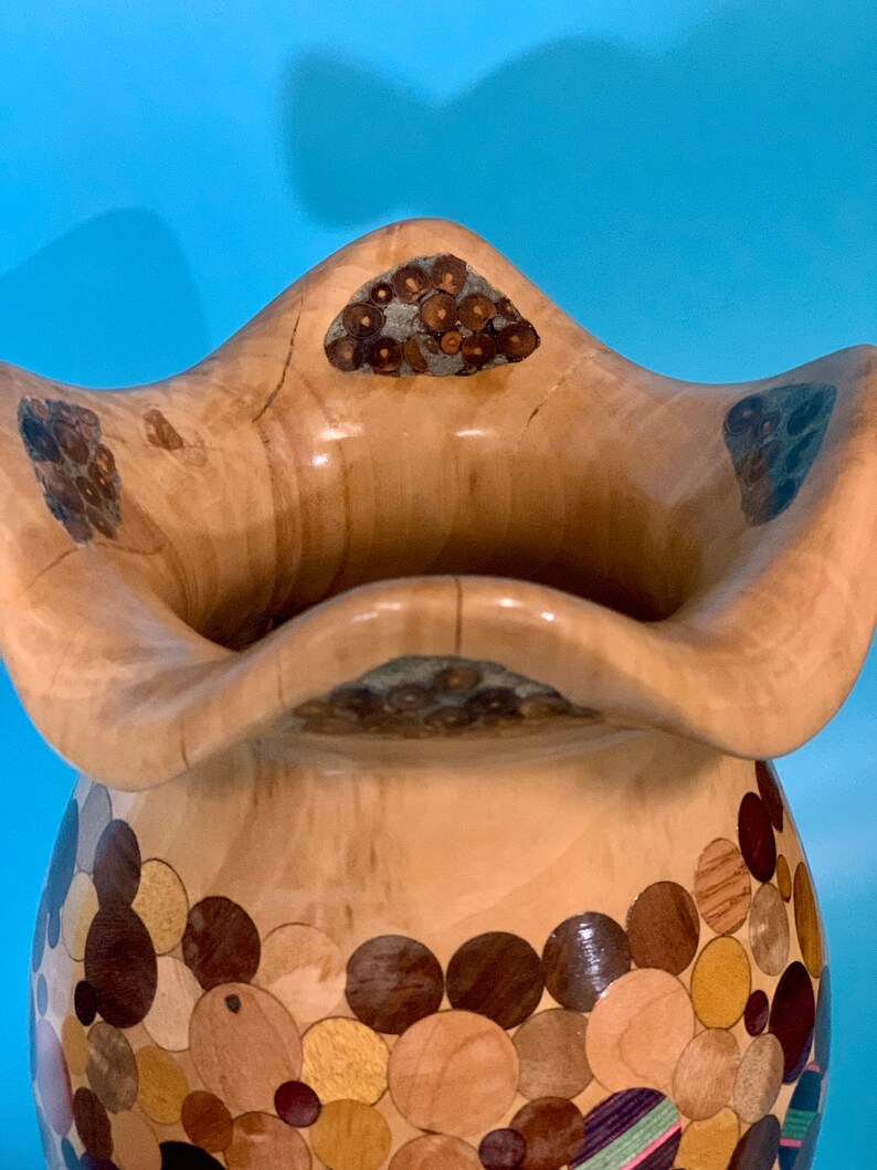 Puede incluir: Un jarr&oacute;n de madera con un dise&ntilde;o &uacute;nico. El jarr&oacute;n est&aacute; hecho de varias piezas de madera, cada una con un color y una veta diferentes. El jarr&oacute;n tiene una boca ancha y una base estrecha. El jarr&oacute;n es una hermosa y &uacute;nica obra de arte.
