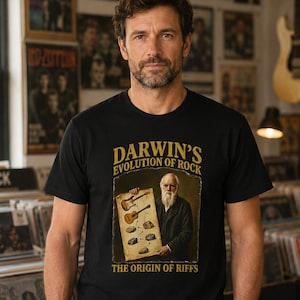 May include: A black t-shirt featuring a graphic of Charles Darwin holding a chart that shows the evolution of musical instruments into electric guitars. The text reads Darwin's Evolution of Rock and The Origin of Riffs in a gold-colored font.