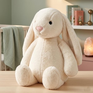 May include: A large, plush cream-colored bunny rabbit with long, floppy ears and a pink nose. The stuffed animal is sitting upright on a wooden surface. The bunny has black eyes and a soft, textured appearance, perfect for a nursery or child's room.