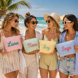 May include: Four rectangular zippered pouches with striped fabric textures. The pink pouch features the name Luna in green, the light green pouch says Nora in pink, the yellow pouch says Ivy in green, and the blue pouch says Sage in pink.