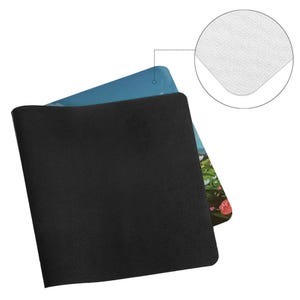 K&ouml;nnte beinhalten: Eine schwarze, rechteckige Mausunterlage mit strukturierter Oberfl&auml;che, die ein farbenfrohes Druckdesign teilweise verdeckt. Das Design zeigt eine Landschaft mit Blumen und blauem Himmel. Eine Nahaufnahme zeigt die wei&szlig;e, glatte Oberfl&auml;che der Mausunterlage.