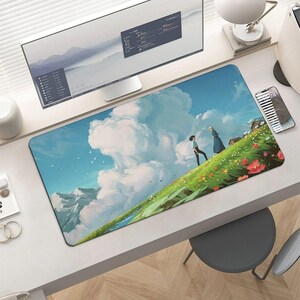 K&ouml;nnte beinhalten: Rechteckiges Mauspad mit einer Anime-Illustration eines grasbewachsenen H&uuml;gels mit Blumen, zwei Figuren und einem bew&ouml;lkten Himmel. Das Design beinhaltet eine Bergkette im Hintergrund. Das Mauspad liegt auf einem wei&szlig;en Schreibtisch mit einem Computermonitor.