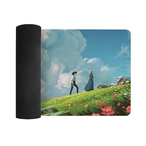 K&ouml;nnte beinhalten: Aufgerollte rechteckige Matte mit einer farbenfrohen Illustration von zwei Figuren auf einem grasbewachsenen H&uuml;gel mit Blumen unter einem blauen Himmel mit flauschigen Wolken. Das Kunstwerk hat einen skurrilen, animierten Stil, mit einer schwarzen, strukturierten Unterseite.