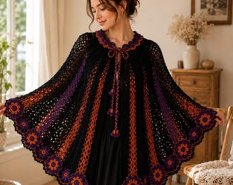 May include: A black crochet cape featuring vertical stripes in orange and purple, a scalloped hem adorned with orange and purple floral motifs, and a tie closure at the neckline with matching purple and orange tassel accents.