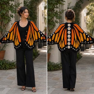 May include: A crochet cardigan featuring a monarch butterfly wing pattern in vibrant orange, black, and white. The front includes three brown buttons, while the back displays a vertical row of white daisy motifs along the centre spine area.