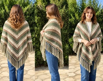 May include: A triangular crochet shawl featuring a chevron pattern in alternating stripes of olive green, cream, and brown yarn. The garment is finished with long, dangling fringe along the bottom edges, creating a textured, layered appearance.