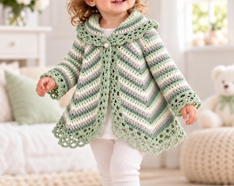 May include: A long-sleeved crochet cardigan featuring a chevron pattern in shades of sage green, cream, and white. The garment has a wide, scalloped collar and hem, with a single pearl-like button closure at the neckline. A matching green bow hair clip.