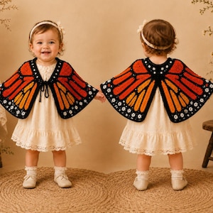 May include: A crochet capelet designed to resemble monarch butterfly wings, featuring vibrant orange and black segments with small white floral accents along the edges. The garment is worn over a cream-colored dress with a lace-trimmed hemline.