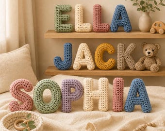 May include: A collection of plush, crocheted letters spelling ELLA, JACK, and SOPHIA. The letters are in various colours including sage green, cream, dusty rose, blue, and yellow. A crocheted teddy bear and a small wooden toy are also visible.