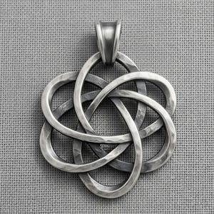 Puede incluir: Un colgante de metal plateado con un diseño de nudo intrincado y entrelazado con un acabado martillado y texturizado. El colgante tiene una forma redondeada y simétrica con seis bucles superpuestos y una anilla curva y lisa en la parte superior.
