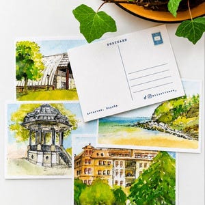Puede incluir: Una colección de cuatro postales rectangulares con ilustraciones en acuarela de paisajes y arquitectura de Asturias, España. Una postal muestra el reverso con el texto POSTCARD, Asturias, España y nombres de redes sociales.