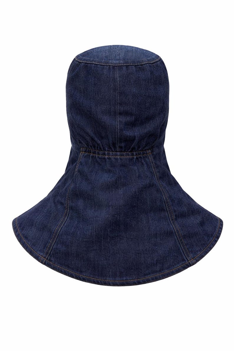 Pu&ograve; includere: Un cappello da sole in denim blu scuro con una tesa larga e un design a forma di cappuccio. Il cappello presenta una corona aderente e una tesa svasata, con dettagli di cucitura visibili. Il tessuto denim sembra essere di peso medio.