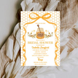 May include: A rectangular bridal shower invitation card featuring a yellow honeycomb pattern border and a central illustration of a honey jar with a dipper. The text reads: She found her, Join us for a bridal shower in honor of Isabella Langford.