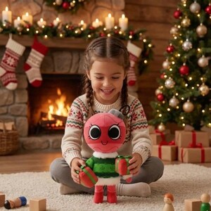 Puede incluir: Una ni&ntilde;a sonriente sostiene un juguete de peluche rojo y verde con ojos grandes y un regalo. El fondo incluye un &aacute;rbol de Navidad decorado, una chimenea con calcetines y regalos envueltos, creando una escena festiva navide&ntilde;a.