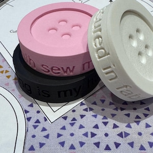 May include: Three large, round buttons in pink, black, and white. The pink button has the words "with sew me" engraved on the side. The white button has the words "measured in fab" engraved on the side. The black button has the words "ing is my" engraved on the side.