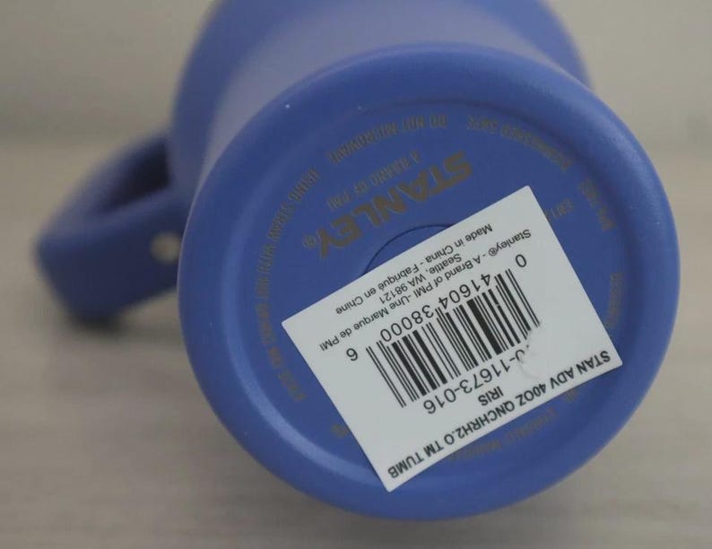 Puede incluir: Un vaso Stanley azul de 40 oz con asa. La parte inferior del vaso tiene una etiqueta blanca con informaci&oacute;n del producto y un c&oacute;digo de barras. Fabricado en China.