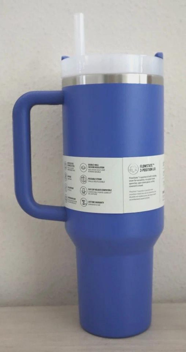 Puede incluir: Un vaso t&eacute;rmico azul con tapa y asa blancas. El vaso tiene una pajita blanca y un borde de acero inoxidable. Una etiqueta en el lateral enumera caracter&iacute;sticas como aislamiento al vac&iacute;o de doble pared y pajita reutilizable. La tapa est&aacute; etiquetada como "FlowState 3-Position Lid."