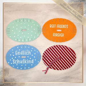 May include: Four oval-shaped yarn weaving looms with notched edges and a central rectangular slot. One is mint green with white dots, one orange with the text BEST FRIENDS FOREVER, one blue with white dots and the text Endlich Schulkind, and one red-striped.