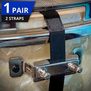Puede incluir: Primer plano de un tambor con una correa negra sujeta a los herrajes del tambor. El tambor tiene una carcasa de color crema con herrajes cromados. El texto "1 Pair" y "2 Straps" está en una pancarta azul.