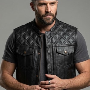 May include: A black leather vest featuring a diamond-quilted pattern on the upper chest and shoulders. The garment includes a front zipper closure, a mandarin collar, and two chest pockets with flaps secured by metallic buttons.