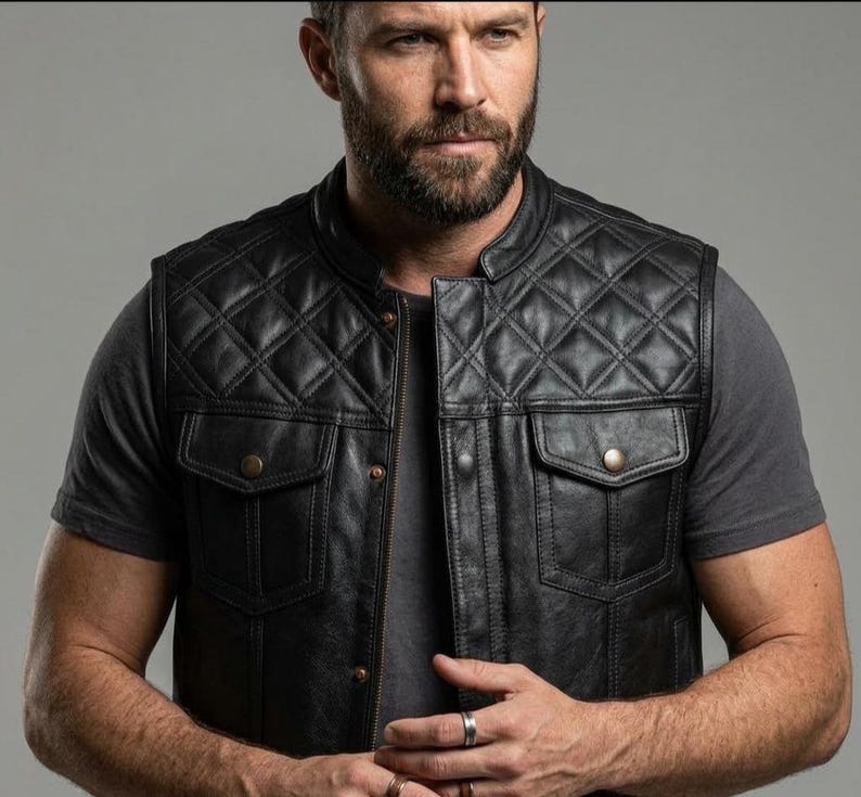 May include: A black leather vest featuring a diamond-quilted pattern on the upper chest and shoulders. The garment includes a front zipper closure, a mandarin collar, and two chest pockets with flaps secured by metallic buttons.