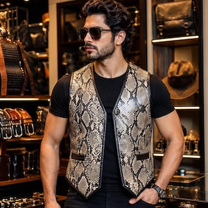 Peut inclure: Un gilet sans manches avec un motif peau de serpent dans des tons beige, marron et noir. Le vêtement présente une encolure en V, des bordures sombres et deux poches avant. Il est porté sur un t-shirt noir uni à manches courtes.