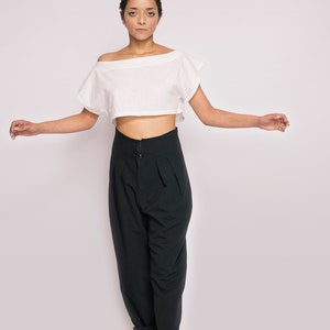 K&ouml;nnte beinhalten: Eine Person tr&auml;gt ein wei&szlig;es, schulterfreies Crop-Top und eine schwarze, hochgeschlossene Hose mit weitem Bein. Sie tr&auml;gt schwarze Sandalen.