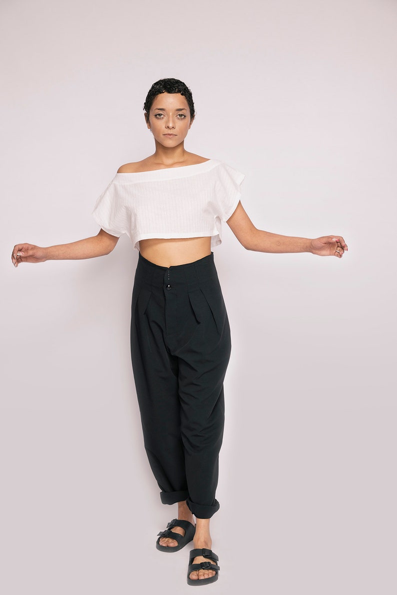 K&ouml;nnte beinhalten: Eine Person tr&auml;gt ein wei&szlig;es, schulterfreies Crop-Top und eine schwarze, hochgeschlossene Hose mit weitem Bein. Sie tr&auml;gt schwarze Sandalen.