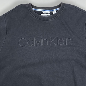 May include: A black Calvin Klein sweatshirt with the brand name embroidered across the chest. The crew neck has a white and blue stripe detail. The garment is made of a soft material.