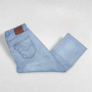 May include: Light blue denim jeans with a classic five-pocket design. Features a brown leather patch on the back and a red tag on the back pocket. The jeans are folded and laid flat.