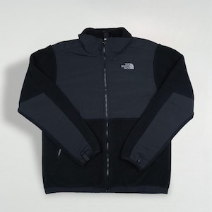 Peut inclure: Veste polaire zippée noire et bleu marine. La veste a un col montant, une fermeture éclair sur toute la longueur et le logo de la marque sur la poitrine. Les manches et le bas du corps sont noirs, tandis que le haut de la poitrine et les épaules sont bleu marine.