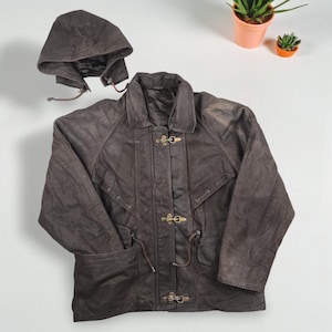 May include: A brown leather jacket with a detachable hood. The jacket features a collared neckline, toggle closures, and pockets. The jacket is displayed on a white background.