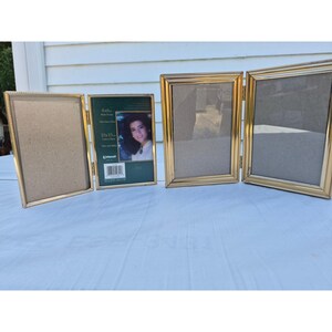 May include: A gold-toned metal triple photo frame with hinged panels. The frames feature a thin, beaded border design. One frame contains a green insert with the text 4x6 in, 10x15 cm, and a photograph of a person. The other three frames are empty.