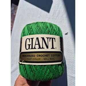 May include: A ball of bright green mercerized crochet cotton yarn with a paper label wrapped around the center. The label features the word GIANT in large black letters, followed by the text MERCERIZED CROCHET COTTON, FAST COLOR, WILL BOIL.